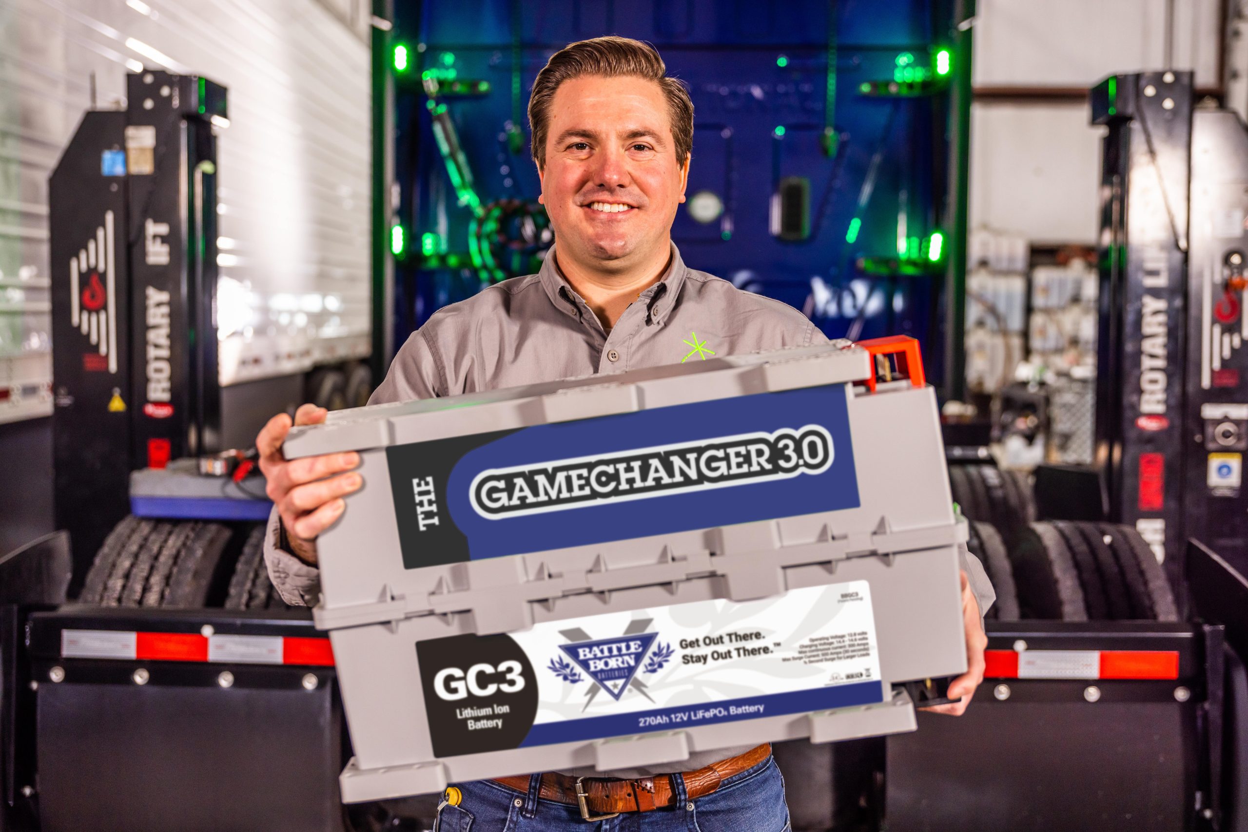 Trucking expert, DJ Hasler standing and smiling in front of a semi-truck holding a Battle Born GC3 Battery.